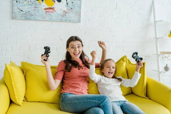 KYIV, UKRAINE - SEPTEMBER 4, 2019: cheerful babysitter and excited kid celebrating triumph while holding joysticks in living room — Stock Photo