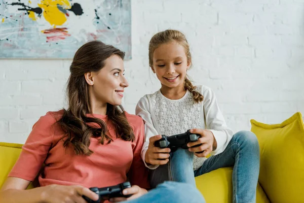 KYIV, UCRANIA - 4 de septiembre de 2019: niñera mirando a un niño feliz jugando videojuegos en la sala de estar - foto de stock
