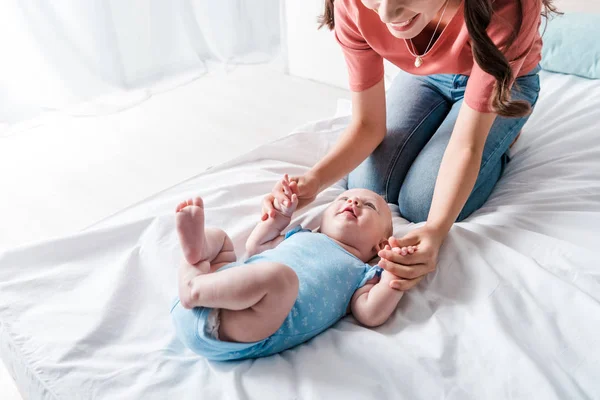 Обрізаний вид щасливої матері, що сидить біля милої дочки-немовляти в блакитному костюмі для немовлят — стокове фото