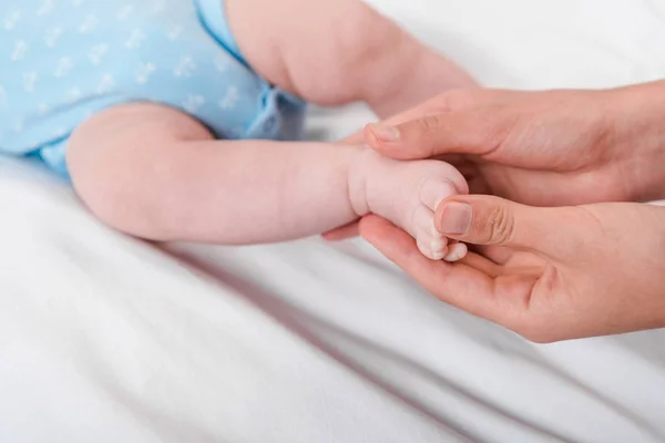 Cropped view of woman touching legs of infant while doing massage — Stock Photo