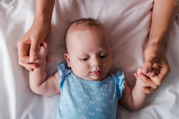 Vista recortada de la madre cogida de la mano en el bebé en traje de bebé - foto de stock