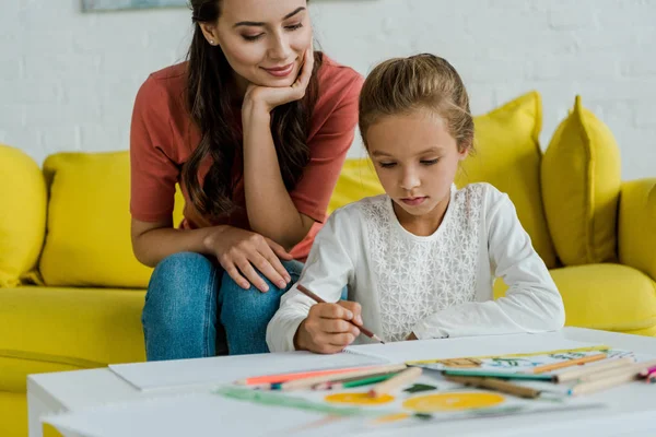 Selektiver Fokus glücklicher Babysitter auf gelbem Sofa in der Nähe von Kinderzeichnungen im Wohnzimmer — Stockfoto