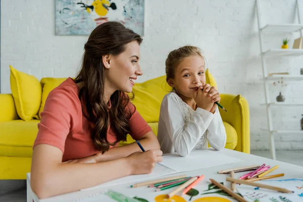 Selective focus of cheerful babysitter looking at cute kid in living room — Stock Photo