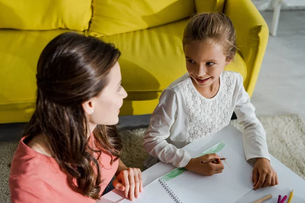 Vue aérienne de baby-sitter joyeux regardant mignon enfant dans le salon — Photo de stock