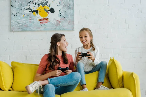 Kyiv, ukraine - 4. September 2019: überraschter Babysitter schaut glückliches Kind beim Videospiel im Wohnzimmer an — Stockfoto