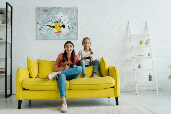 KYIV, UCRANIA - 4 de septiembre de 2019: niñera emocionada y niño feliz jugando videojuegos en la sala de estar - foto de stock