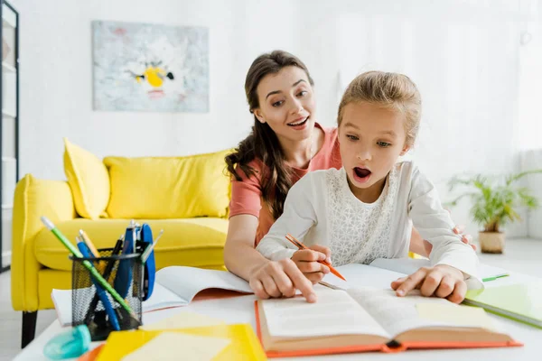 Selektiver Fokus des glücklichen Babysitters, der mit dem Finger auf Buch zeigt, in der Nähe eines überraschten Kindes — Stockfoto