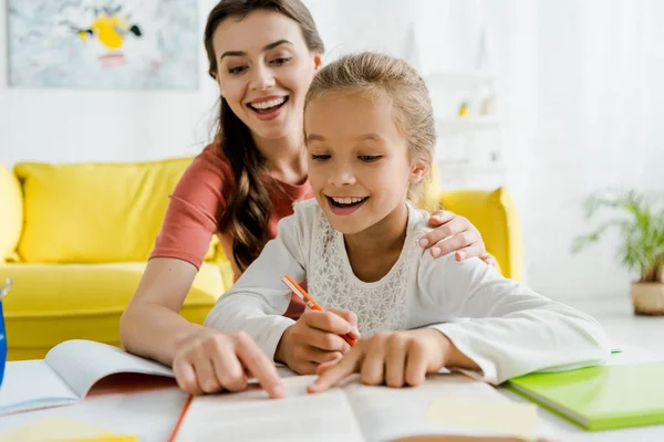 Selective focus of happy babysitter and cheerful kid pointing with fingers at book — Stock Photo