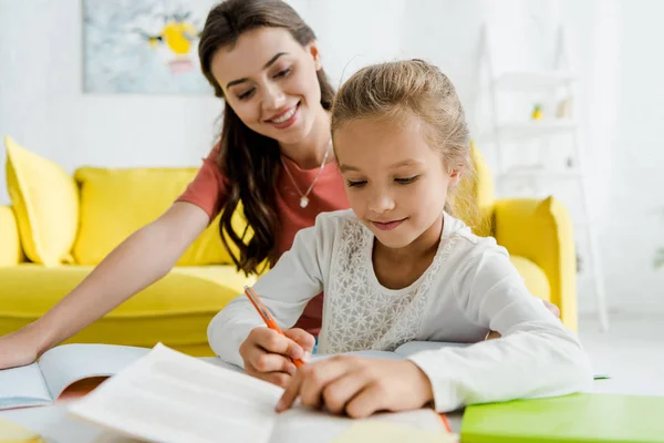 Enfoque selectivo de niño feliz estudiando cerca de niñera en casa - foto de stock