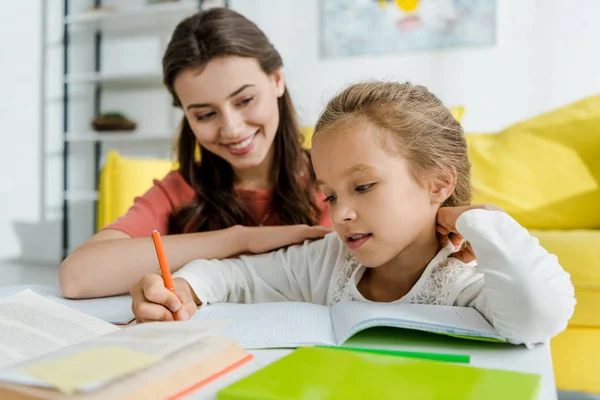 Enfoque selectivo de lindo niño estudiando cerca de niñera feliz en casa - foto de stock