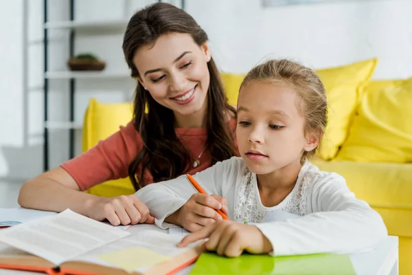 Messa a fuoco selettiva del bambino carino che punta con il dito al libro vicino alla babysitter allegra a casa — Foto stock