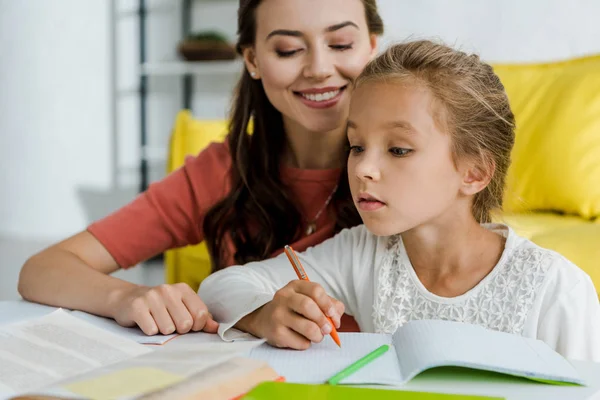 Selective focus of cute kid studying near cheerful babysitter at home — Stock Photo