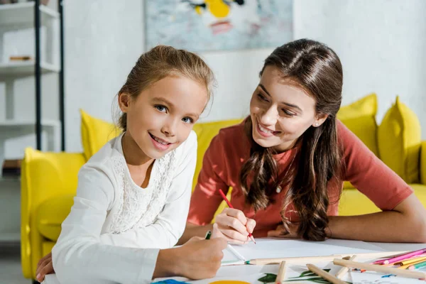 Niñera feliz mirando lindo niño sonriendo en sala de estar - foto de stock