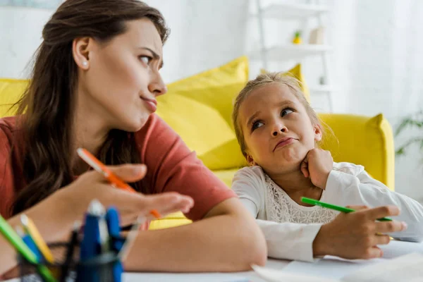 Enfoque selectivo de la niñera mostrando gesto de encogimiento mientras mira al niño - foto de stock