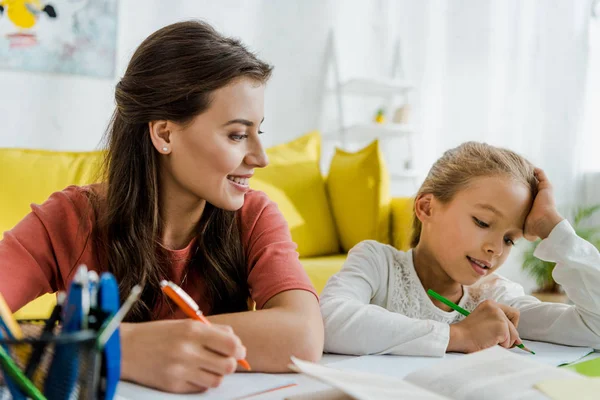 Messa a fuoco selettiva di babysitter felice guardando bambino che studia in soggiorno — Foto stock