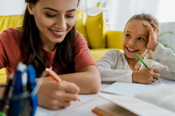 Selektiver Fokus glücklicher Kinder, die fröhliche Babysitterin mit Stift im Wohnzimmer betrachten — Stockfoto