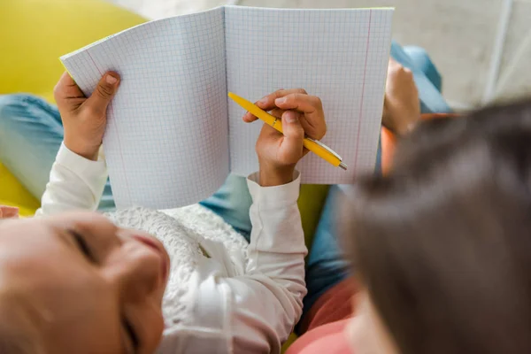 Selektiver Fokus des glücklichen Kindes mit Notizbuch und Blick auf Babysitter im Wohnzimmer — Stockfoto