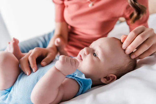 Vista recortada de la madre tocando la cabeza del bebé lindo en el dormitorio - foto de stock