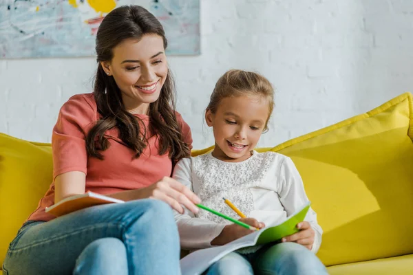 Selective focus of happy babysitter with pencil sitting near kid in living room — Stock Photo