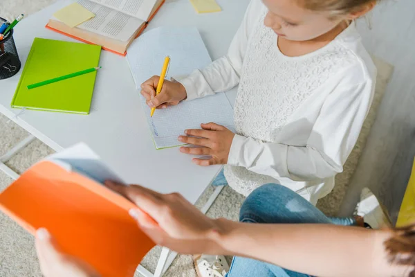 Vista aérea de niñera sosteniendo portátil cerca de niño lindo estudiando en casa - foto de stock