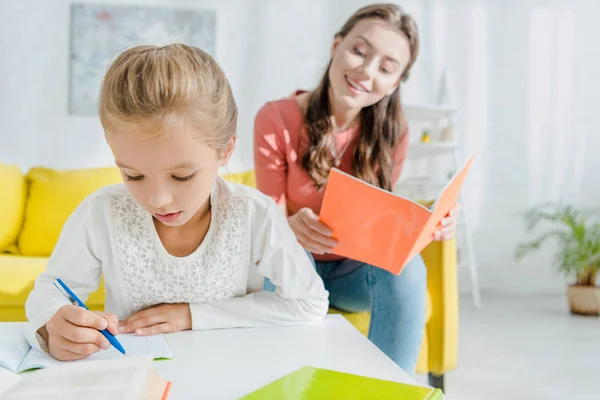 Selective focus of cute child studying near attractive babysitter at home — Stock Photo