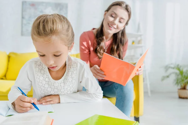 Enfoque selectivo de lindo niño estudiando cerca atractiva niñera en casa - foto de stock