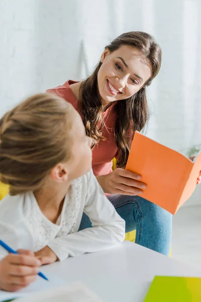 Selective focus of child studying near attractive babysitter at home — Stock Photo