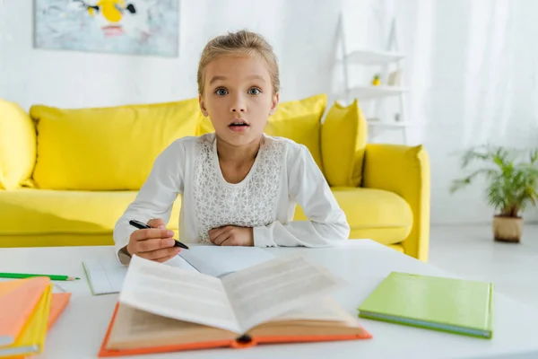 Selective focus of cute and surprised kid looking at camera while studying at home — Stock Photo