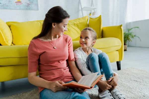 Enfant heureux assis sur le tapis près de baby-sitter avec livre — Photo de stock