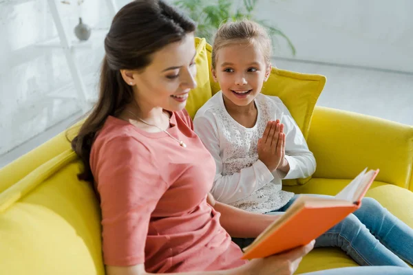 Selective focus of kid with praying hands looking at babysitter reading book — Stock Photo