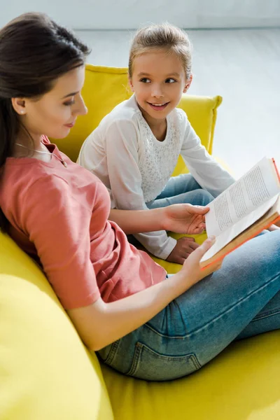 Foyer sélectif de l'enfant regardant le livre de lecture de baby-sitter tout en étant assis sur le canapé — Photo de stock