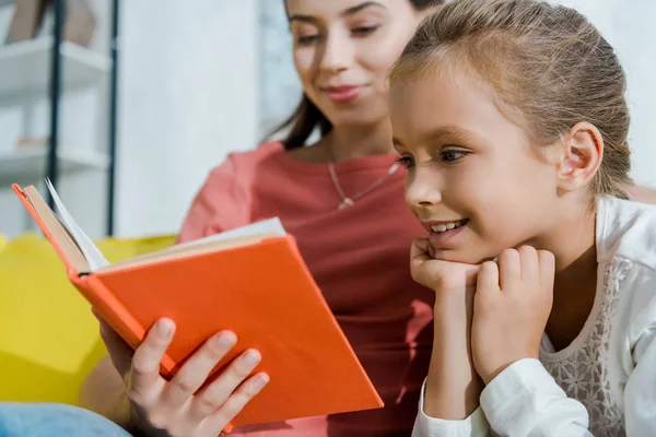 Selective focus of happy kid looking at book near happy babysitter — Stock Photo