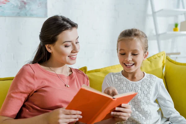 Foco seletivo da criança feliz que olha para o livro em mãos da babá alegre — Fotografia de Stock