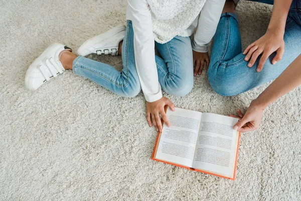 Top view of babysitter sitting on carpet with kid near book — Stock Photo