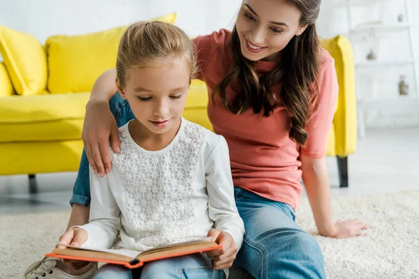 Happy babysitter sitting with cute kid reading book — Stock Photo