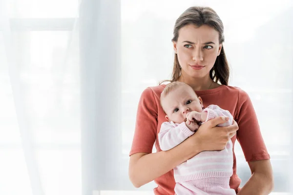 Збентежена мати тримає в руках чарівну доньку-немовля вдома — стокове фото