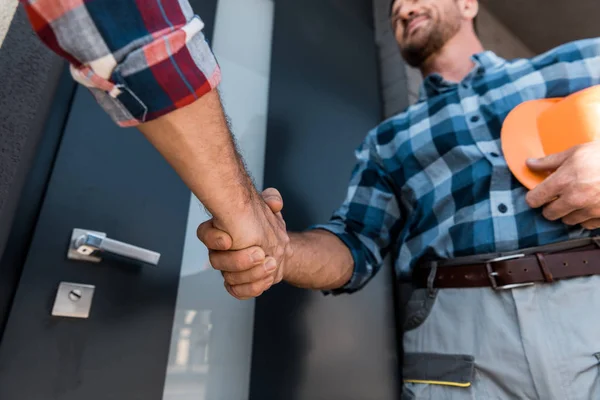 Vista recortada de los hombres estrechando las manos mientras están de pie cerca de la puerta - foto de stock