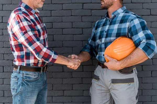 Cropped view of men shaking hands while standing near brick wall — Stock Photo