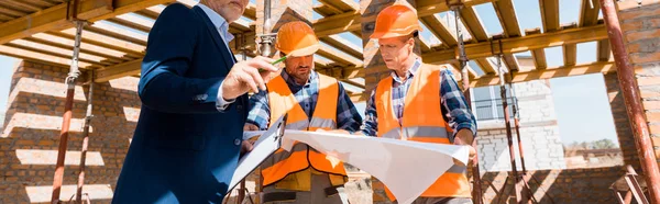 Tiro panorâmico de empresário perto de construtores segurando planta — Fotografia de Stock