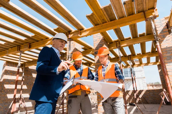 Mature businessman near builders in helmets holding blueprint — Stock Photo