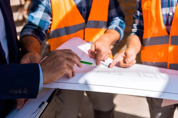 Vue recadrée de l'homme d'affaires tenant crayon près du plan directeur et les constructeurs — Photo de stock