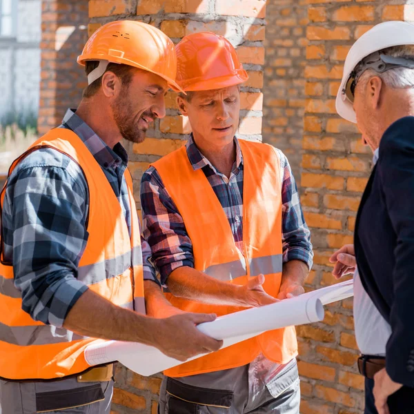 Messa a fuoco selettiva di costruttori vicino uomo d'affari maturo in casco guardando progetto — Foto stock