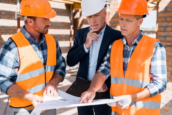 Mature constructor pointing with finger at blueprint near businessman — Stock Photo