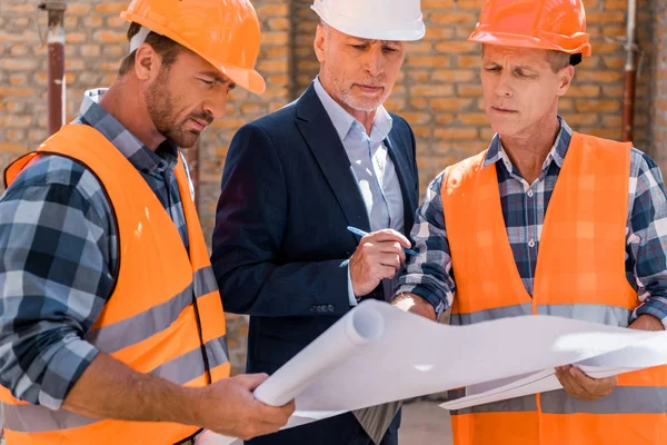 Messa a fuoco selettiva di costruttori e uomo d'affari maturo in giacca e cravatta guardando progetto — Foto stock