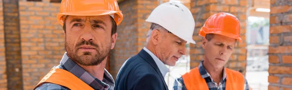 Panoramic shot of constructor in helmet near coworker and businessman — Stock Photo