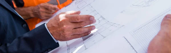 Panoramic shot of businessman gesturing near blueprint and constructors — Stock Photo