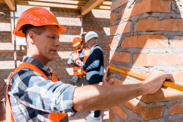 Selective focus of mature constructor measuring building outside — Stock Photo