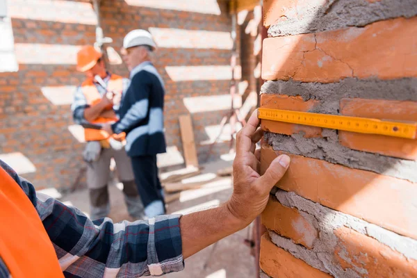 Cropped view of mature man measuring brick wall near coworker and businessman — Stock Photo