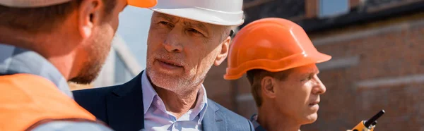 Panoramic shot of constructor near businessman and coworker — Stock Photo