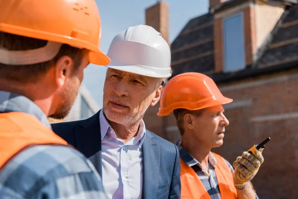 Selective focus of constructor near bearded businessman and coworker in helmets — Stock Photo